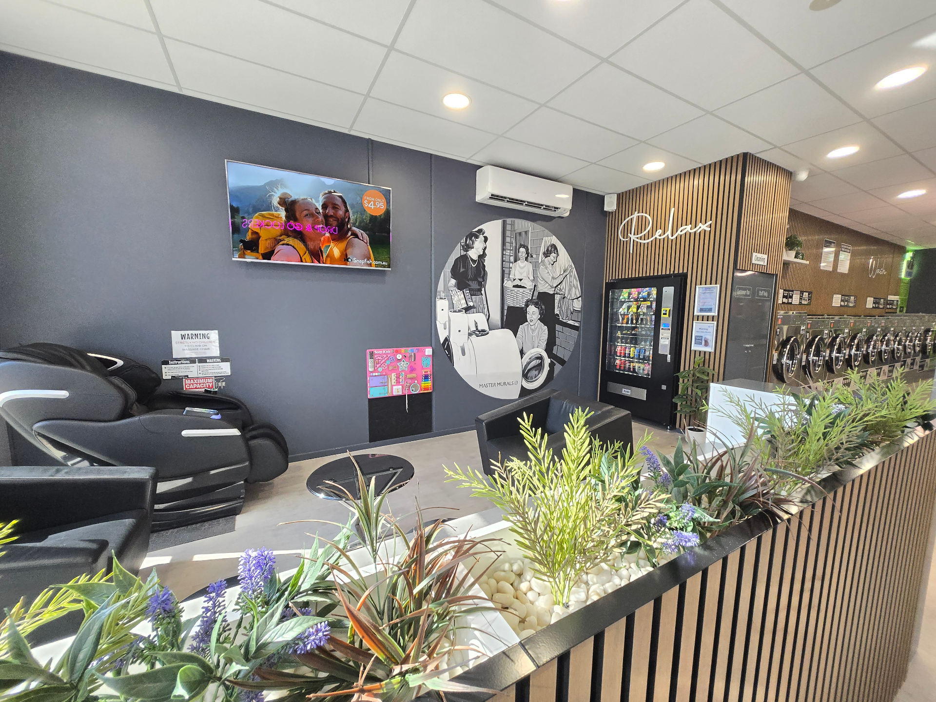 Comfortable customer lounge at Soap Queens Laundry Lounge in Cranbourne North, with massage chair, seating and Relax feature wall